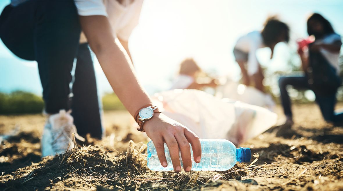 Woman picking up a plastic bottle from the ground, with other litter pickers in the background